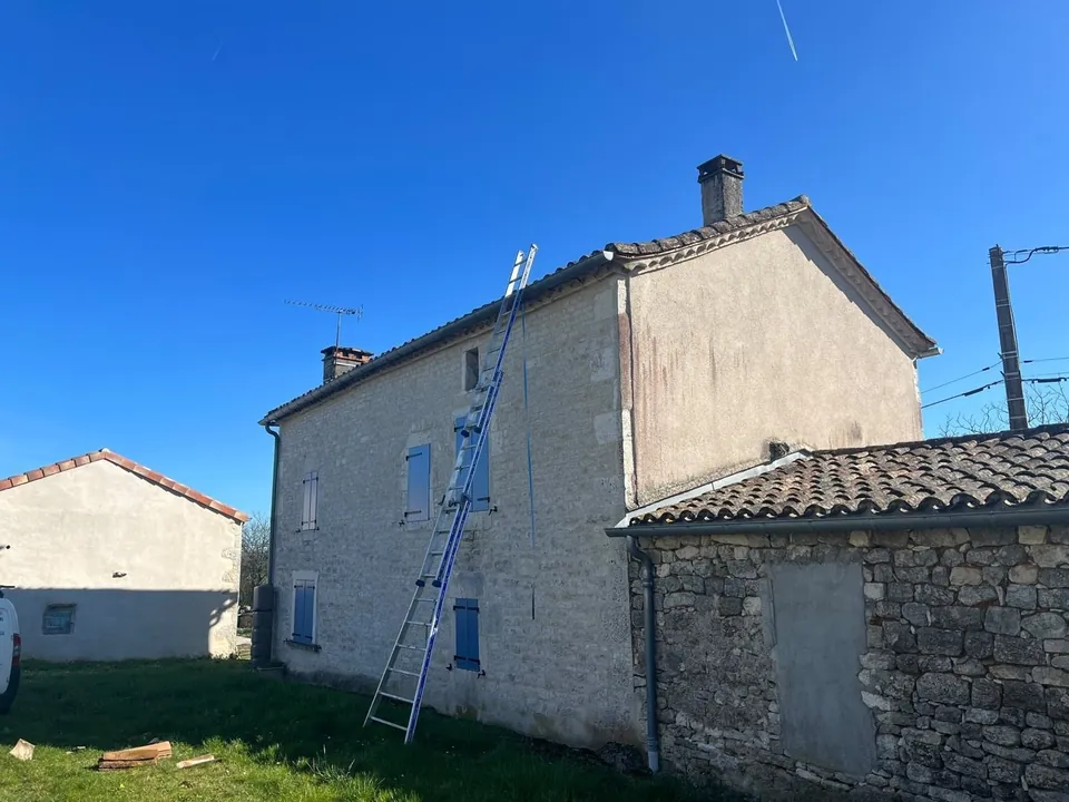 Échelle dressée contre une maison en pierre pour un chantier de toiture